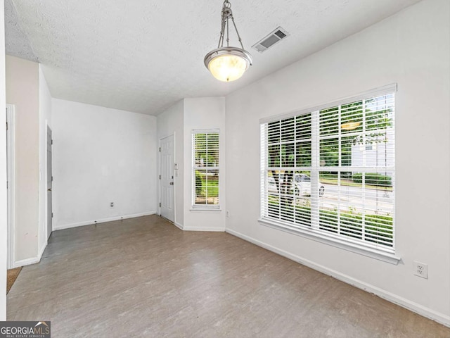 interior space with baseboards, a textured ceiling, visible vents, and wood finished floors