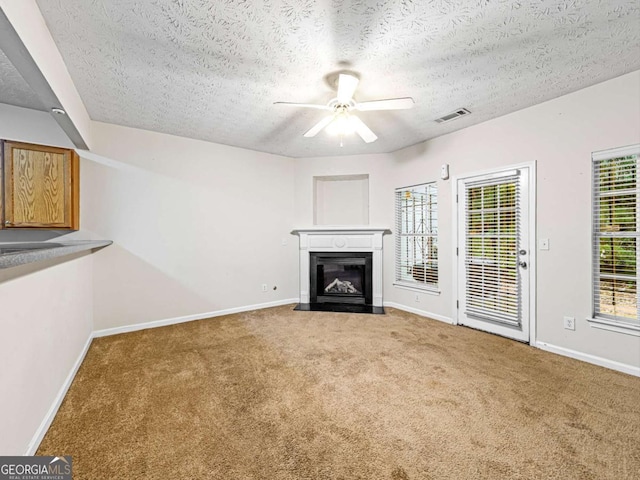 unfurnished living room with carpet floors, a fireplace with flush hearth, a ceiling fan, visible vents, and baseboards