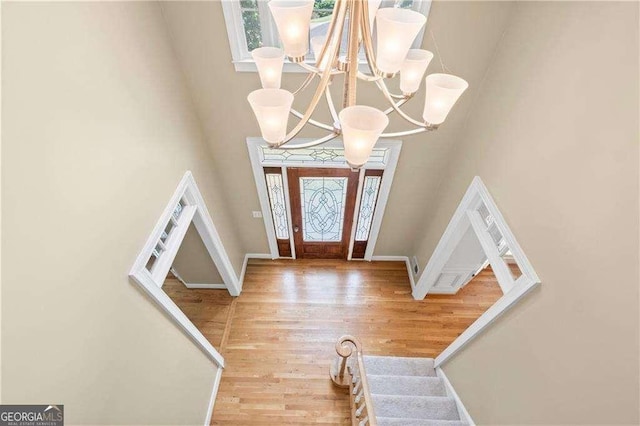 entrance foyer featuring baseboards, a towering ceiling, light wood-style flooring, an inviting chandelier, and stairs