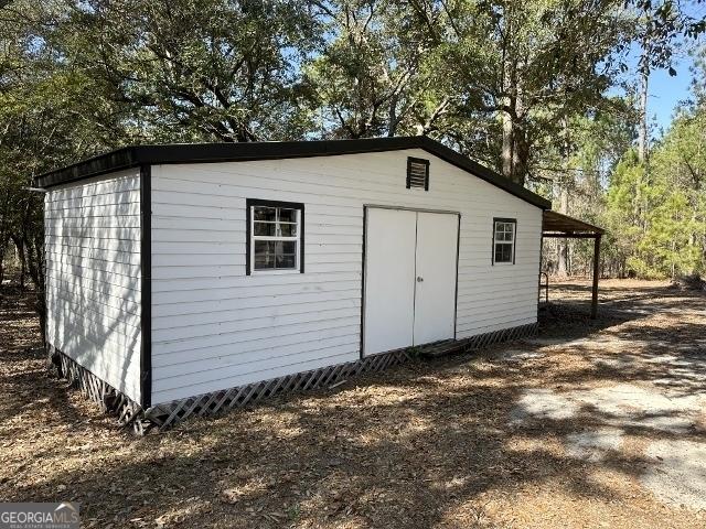 view of outbuilding featuring dirt driveway, a carport, and an outdoor structure