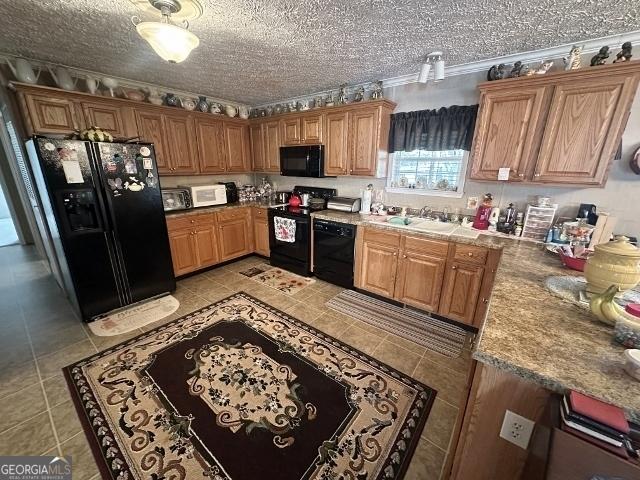 kitchen with a textured ceiling, light tile patterned flooring, a sink, black appliances, and brown cabinetry