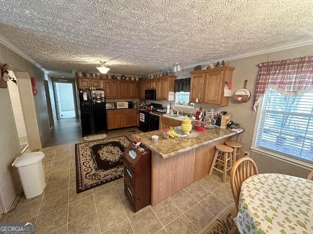 kitchen with a breakfast bar, brown cabinets, crown molding, black appliances, and light tile patterned flooring