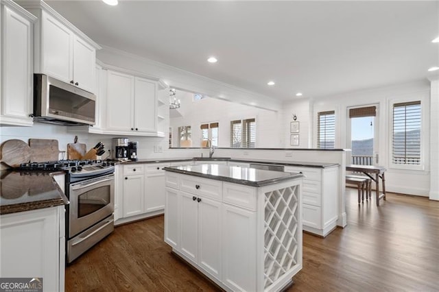 kitchen with stainless steel appliances, white cabinetry, a kitchen island, a sink, and a peninsula