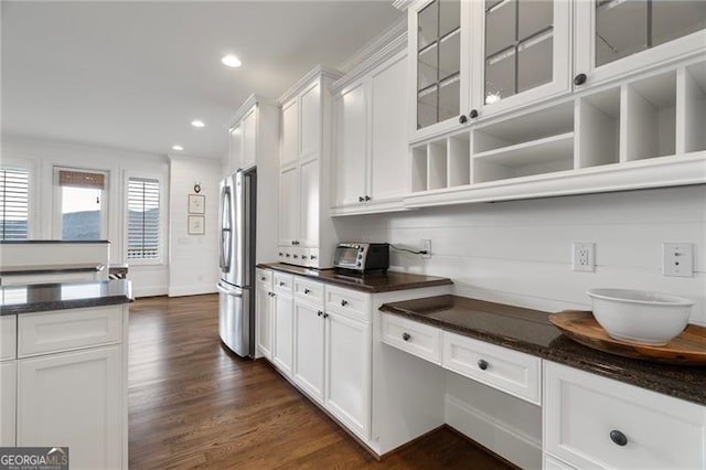 kitchen with glass insert cabinets, dark wood-style flooring, dark stone countertops, freestanding refrigerator, and white cabinetry