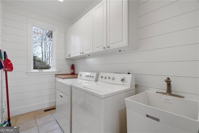 clothes washing area with visible vents, cabinet space, a sink, wood walls, and independent washer and dryer