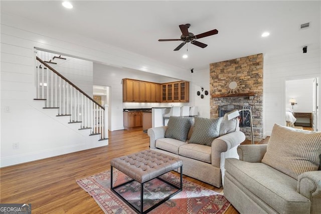 living area with light wood finished floors, recessed lighting, visible vents, a stone fireplace, and stairs