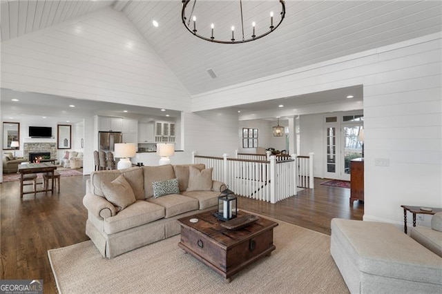 living room featuring a warm lit fireplace, high vaulted ceiling, a chandelier, recessed lighting, and wood finished floors