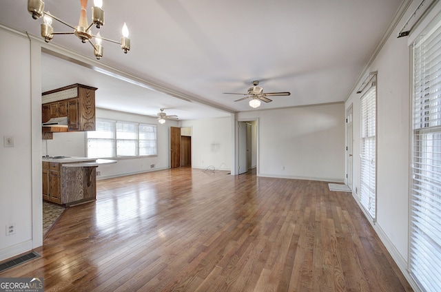 unfurnished living room with hardwood / wood-style flooring, ceiling fan with notable chandelier, visible vents, baseboards, and ornamental molding