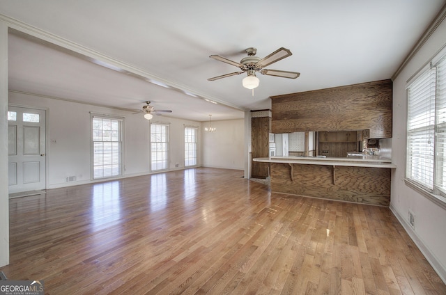 unfurnished living room with a wealth of natural light, wood finished floors, and ceiling fan with notable chandelier