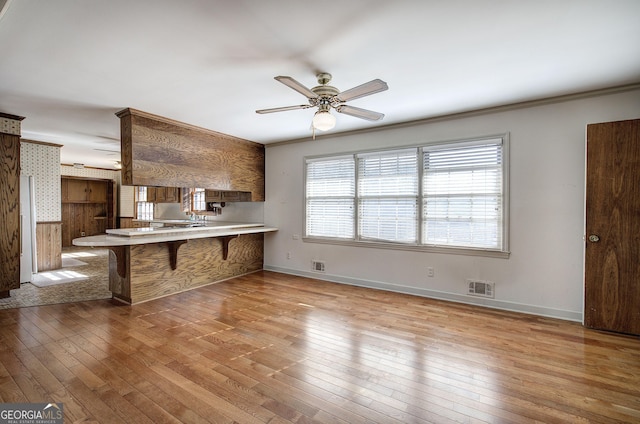 kitchen with a breakfast bar area, wood-type flooring, visible vents, ceiling fan, and a peninsula