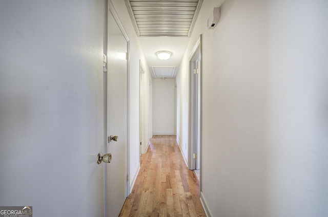 hallway featuring attic access, visible vents, light wood-style flooring, and baseboards