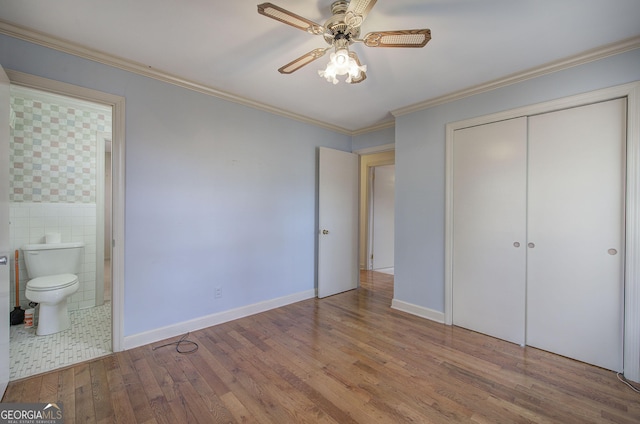 unfurnished bedroom featuring crown molding, tile walls, a closet, ensuite bathroom, and wood finished floors