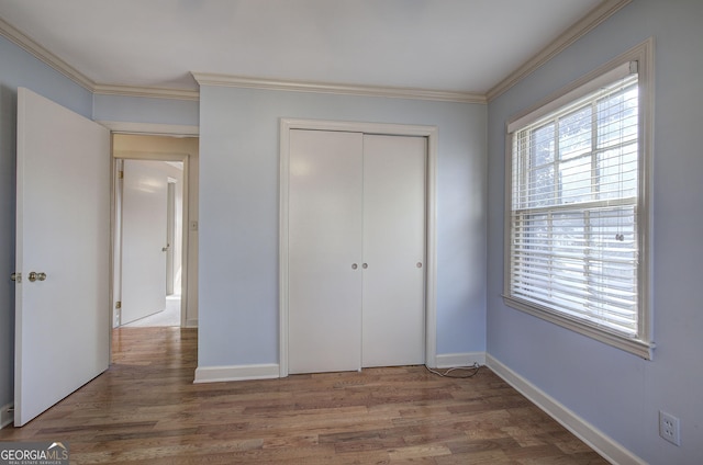 unfurnished bedroom with a closet, crown molding, baseboards, and wood finished floors