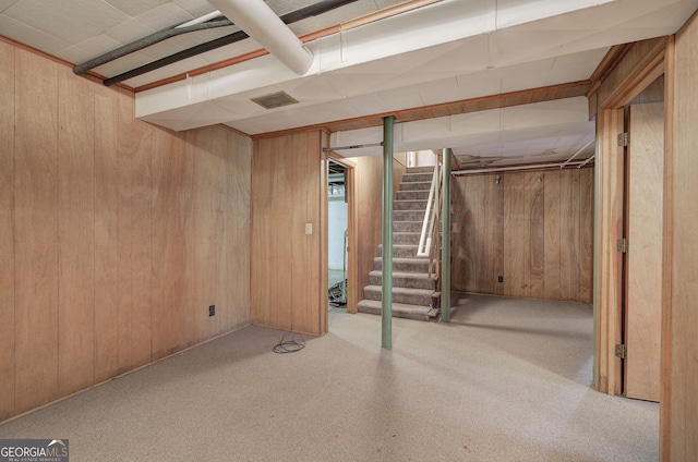 finished basement featuring stairway, wood walls, carpet flooring, and visible vents