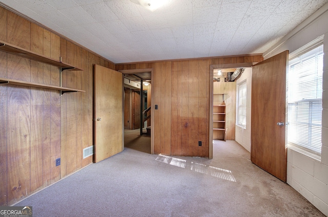 unfurnished bedroom with carpet floors, wood walls, multiple windows, and visible vents