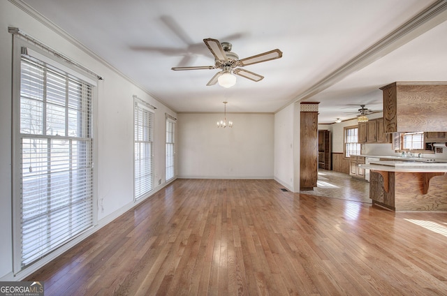 unfurnished living room with light wood-style floors, baseboards, ornamental molding, and ceiling fan with notable chandelier