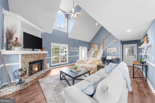 living area with a stone fireplace, wood finished floors, a ceiling fan, baseboards, and stairway