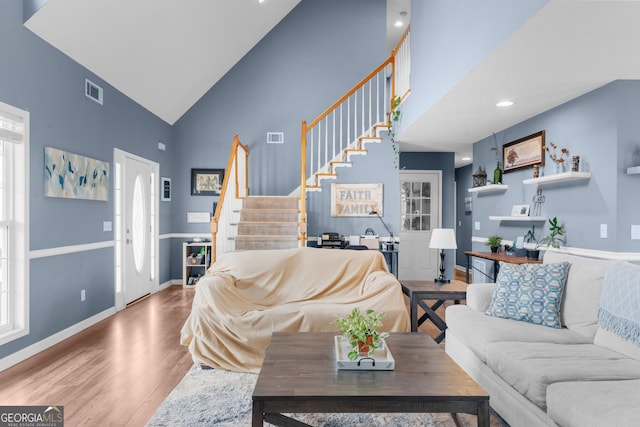 living area with visible vents, stairs, high vaulted ceiling, and wood finished floors