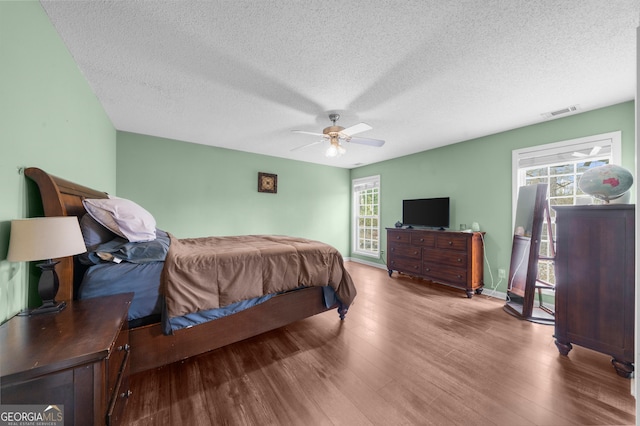 bedroom with a textured ceiling, wood finished floors, visible vents, and a ceiling fan