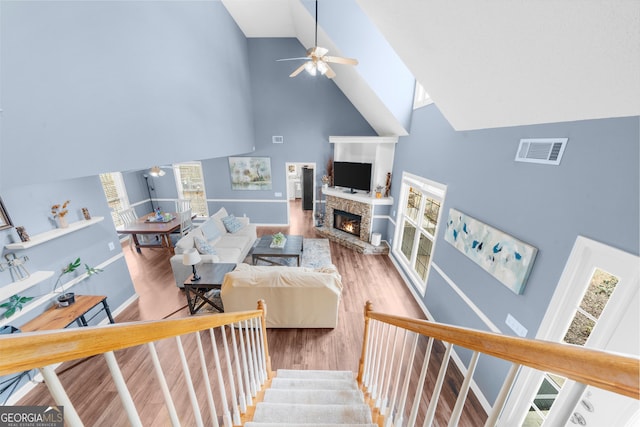 living room featuring high vaulted ceiling, a stone fireplace, wood finished floors, visible vents, and a ceiling fan