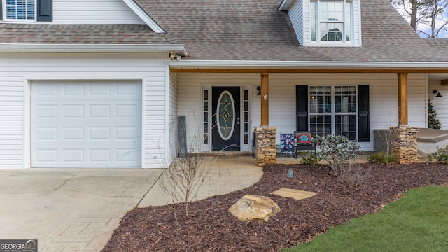 doorway to property featuring an attached garage, covered porch, a shingled roof, and concrete driveway