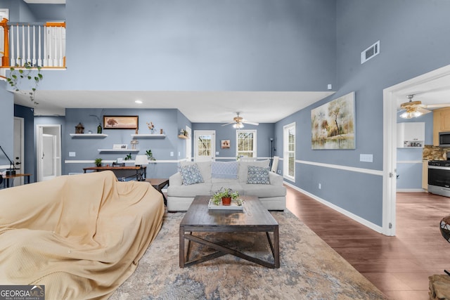 living area featuring baseboards, a high ceiling, visible vents, and wood finished floors