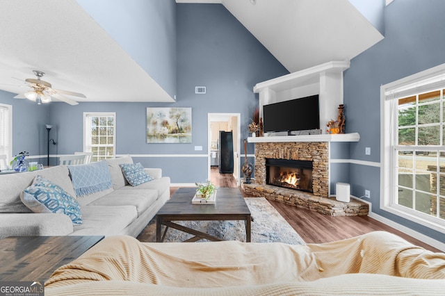 living room with baseboards, visible vents, wood finished floors, a stone fireplace, and high vaulted ceiling