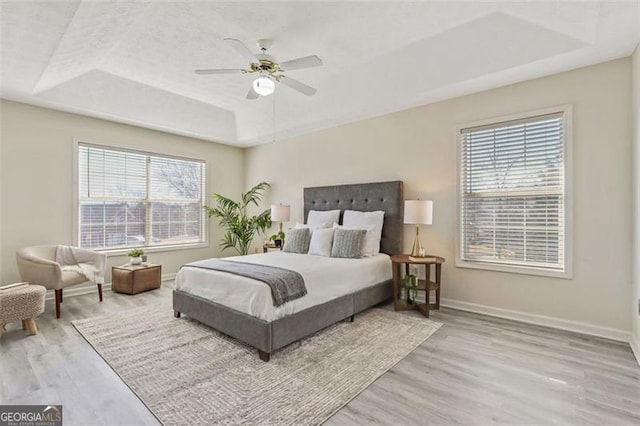 bedroom featuring a raised ceiling, multiple windows, baseboards, and light wood finished floors