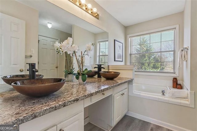 full bath featuring double vanity, wood finished floors, a sink, and a bath