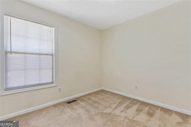 spare room featuring baseboards, visible vents, and light colored carpet