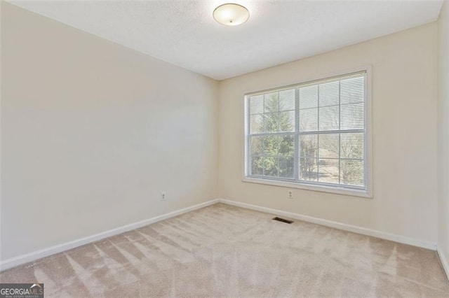 spare room with visible vents, baseboards, a textured ceiling, and light colored carpet