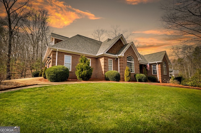 view of front of property with a shingled roof, a lawn, and brick siding