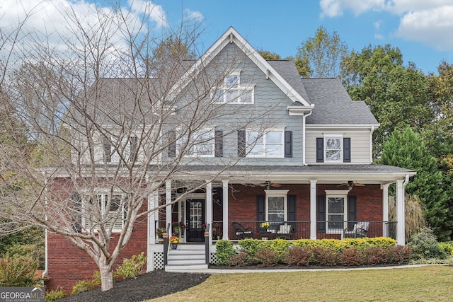 view of front facade with brick siding, a shingled roof, a ceiling fan, covered porch, and a front yard