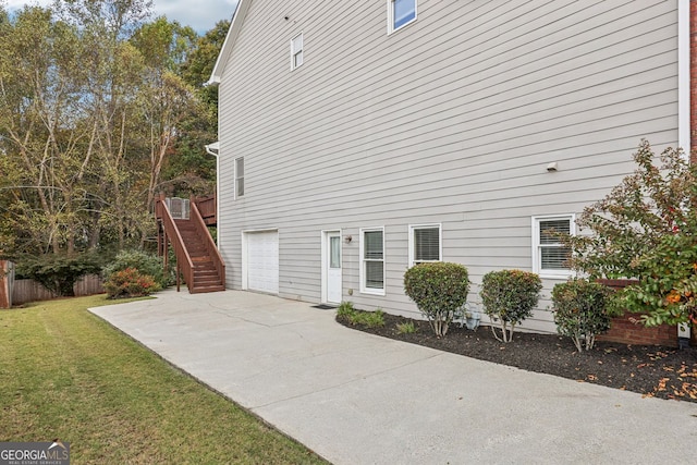 view of side of home featuring a garage, fence, driveway, stairway, and a lawn