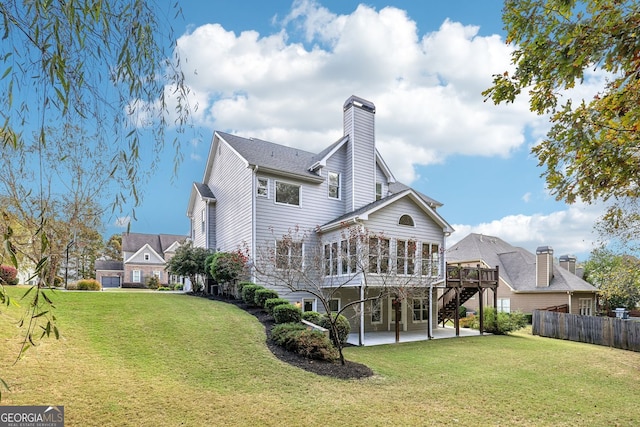 rear view of house featuring a wooden deck, fence, a lawn, and a patio