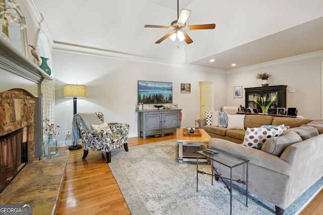 living room featuring ceiling fan, crown molding, a stone fireplace, and wood finished floors