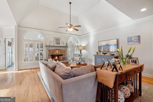 living area featuring ceiling fan, a fireplace, light wood-style floors, vaulted ceiling, and crown molding