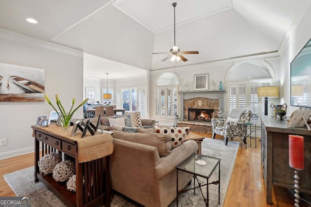 living room with a wealth of natural light, light wood-style flooring, crown molding, and a stone fireplace