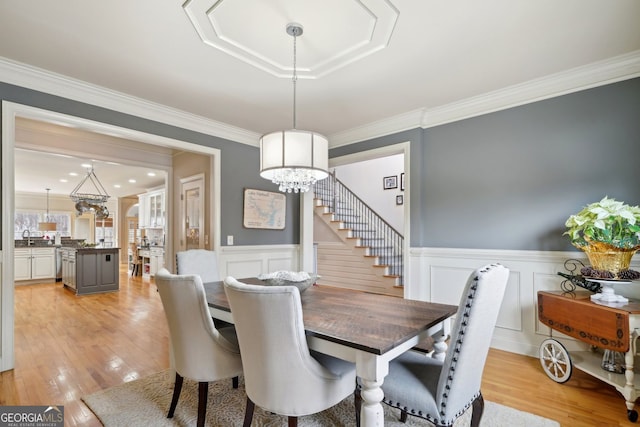 dining space with a chandelier, a wainscoted wall, ornamental molding, stairway, and light wood-type flooring