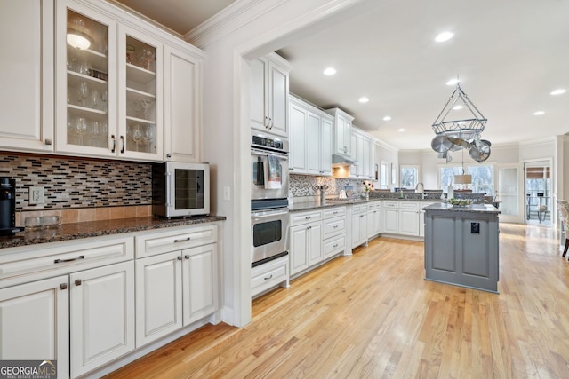 kitchen with glass insert cabinets, white cabinetry, ornamental molding, and light wood-style flooring