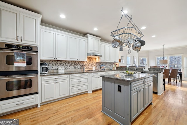 kitchen featuring appliances with stainless steel finishes, a peninsula, gray cabinets, crown molding, and under cabinet range hood