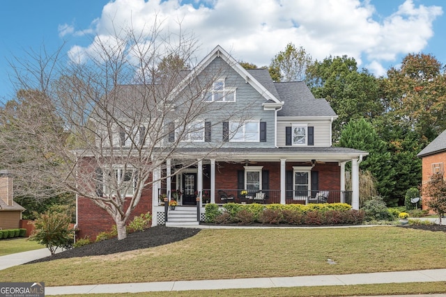 view of front facade with a shingled roof, covered porch, brick siding, and a front lawn