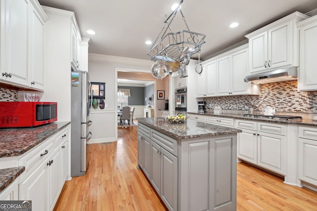 kitchen featuring under cabinet range hood, a kitchen island, white cabinetry, appliances with stainless steel finishes, and crown molding