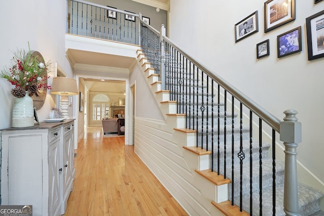 stairway featuring ornamental molding, wainscoting, a high ceiling, and wood finished floors