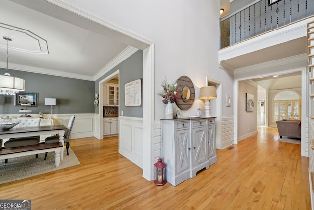 interior space with light wood-type flooring, wainscoting, crown molding, and visible vents