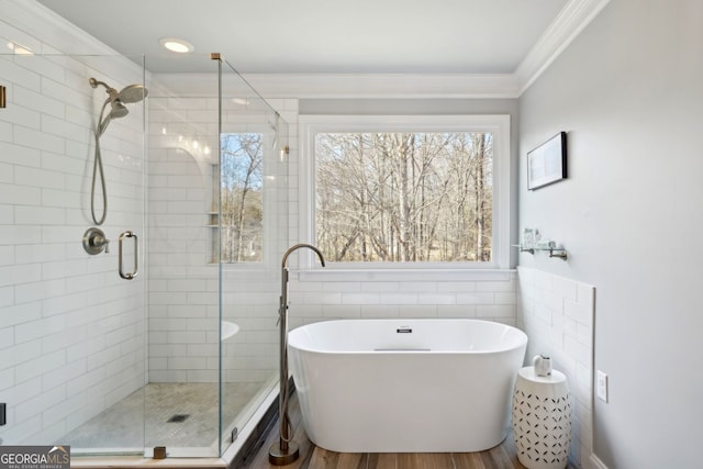 bathroom featuring wood finished floors, ornamental molding, a soaking tub, and a shower stall