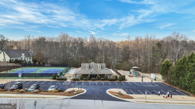 view of property's community with uncovered parking, playground community, a wooded view, and fence