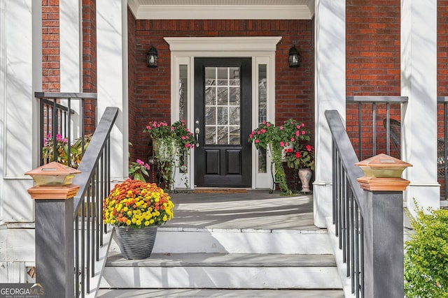 doorway to property featuring a porch and brick siding