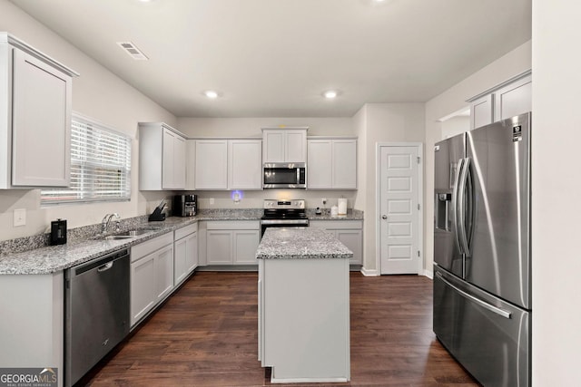 kitchen with light stone counters, stainless steel appliances, a sink, white cabinets, and a center island