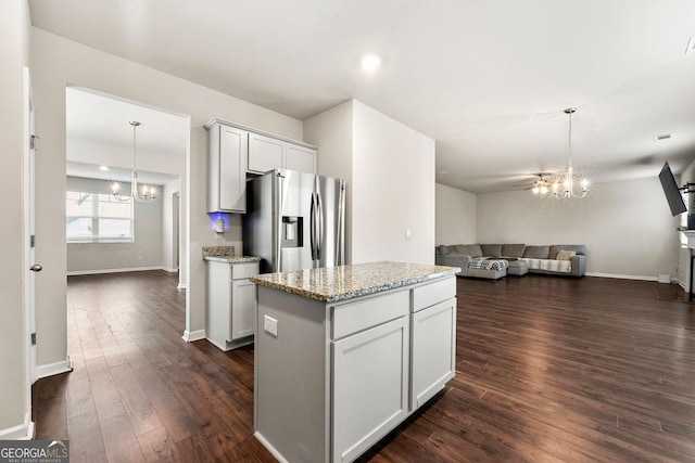 kitchen with stainless steel refrigerator with ice dispenser, a kitchen island, open floor plan, and a notable chandelier